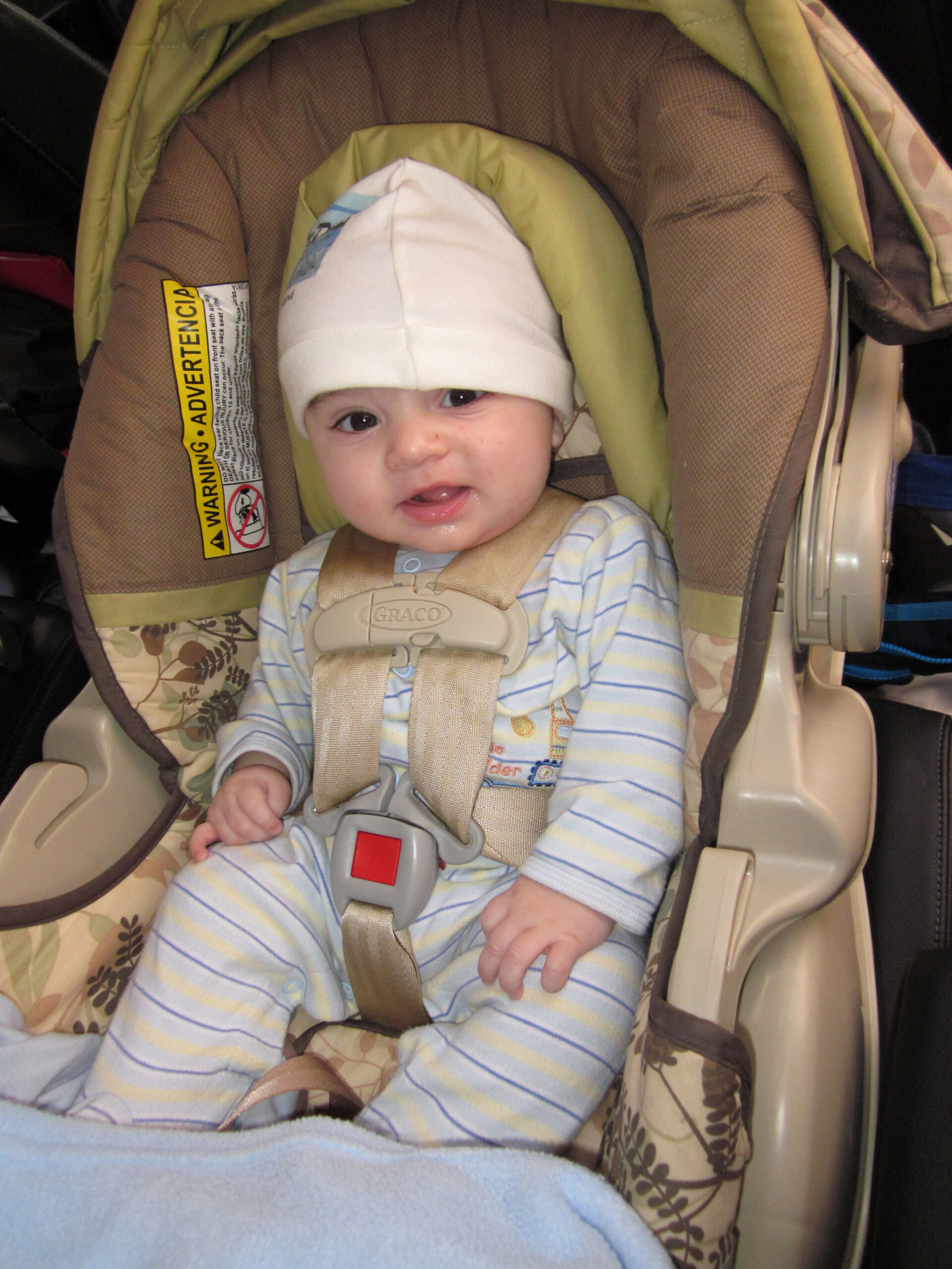 Baby in hat buckled into car seat.
