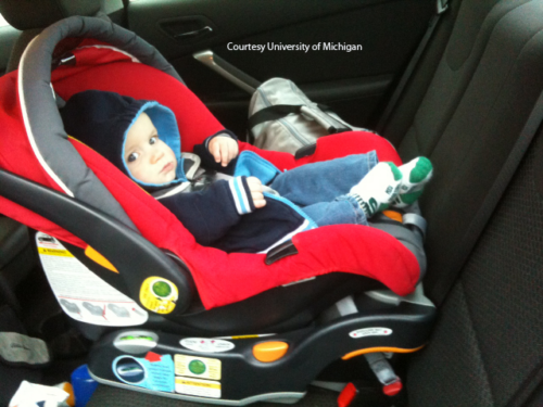 Baby buckled into red backward-facing carseat.